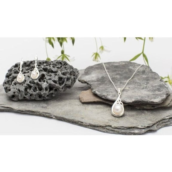 The Trinity Knot Classic Pearl Jewelry Set featuring a pendant necklace and matching earrings. The pendant has a teardrop design with a central freshwater pearl and silver trinity knot accents, while the earrings mirror the pendant's shape.