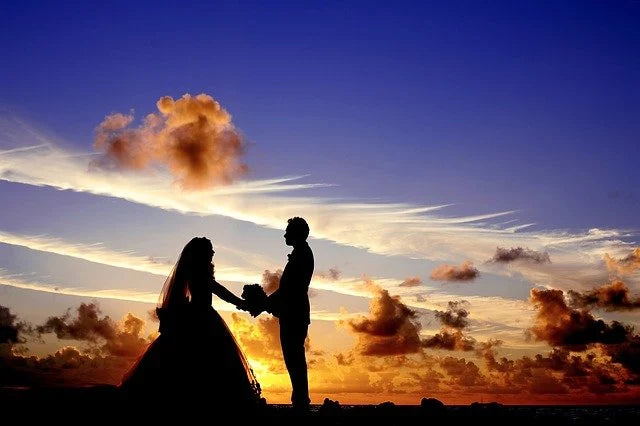 A couple in wedding attire hold hands against a sky at sunset creating a romantic atmosphere