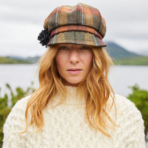 A woman wearing a beige Irish wool newsboy cap with a leather flower motif on the side.