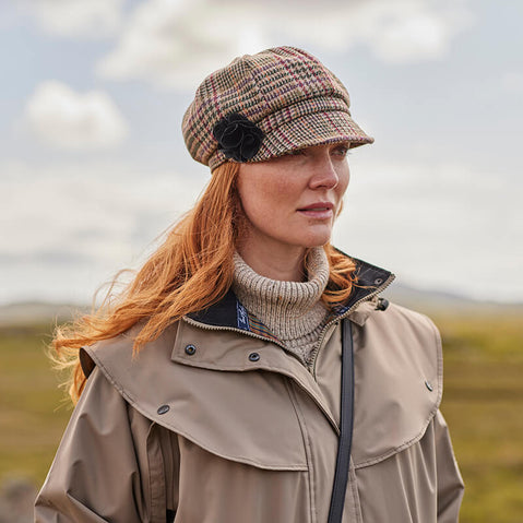 A woman wearing a beige Irish wool newsboy cap with a leather flower motif on the side.