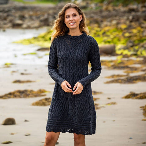 A woman standing on a beach wearing a long sleeve cable knit aran dress in green color.