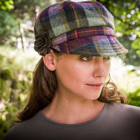 A woman wearing a beige Irish wool newsboy cap with a leather flower motif on the side.