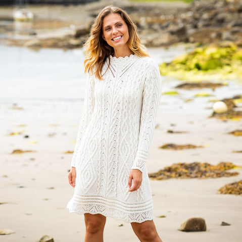 A woman standing on a beach wearing a long sleeve cable knit aran dress in green color.