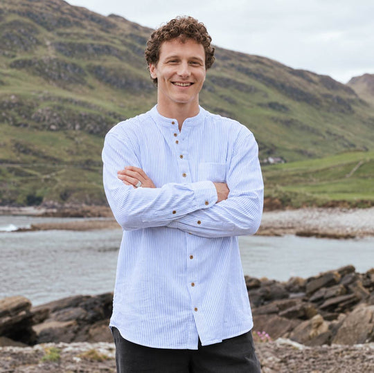 Image featuring the Blue Stripe Grandad Shirt, crafted with a traditional Irish grandad collar, classic blue and white stripe design, button-front placket, and relaxed fit, showcasing timeless Irish style against a scenic coastal landscape.