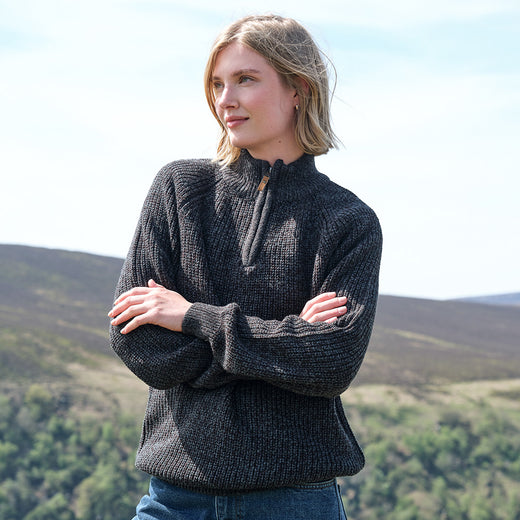 Woman wearing a dark gray knit sweater with a mountainous landscape in the background