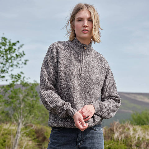 Person wearing a gray knit sweater standing outdoors with a natural background