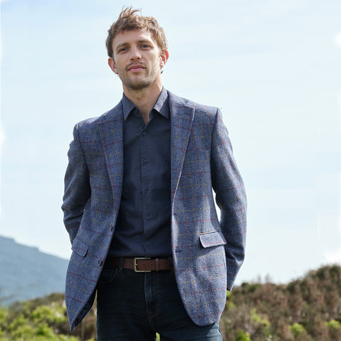 Man wearing a blue checkered tweed blazer over a dark shirt with a blurred natural background