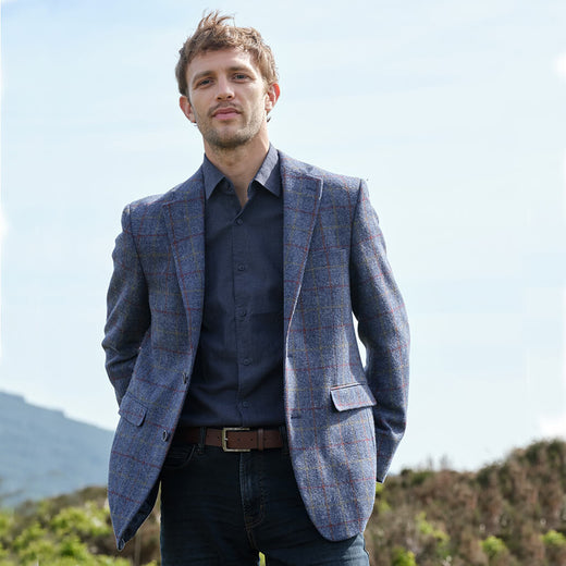 Man wearing a blue checkered tweed blazer over a dark shirt with a blurred natural background