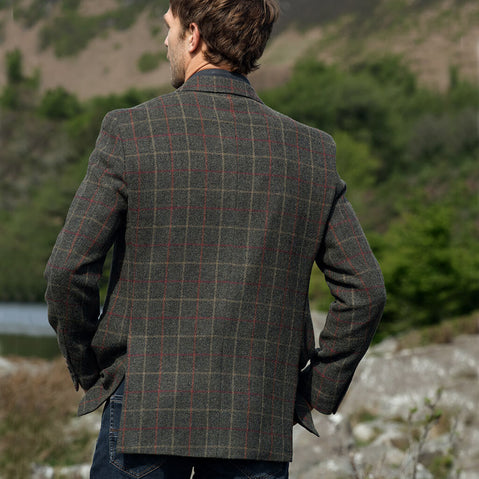 Man wearing a tweed jacket standing outdoors with a natural landscape in the background