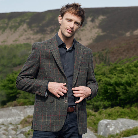 Man wearing a tweed jacket outdoors with mountains in the background