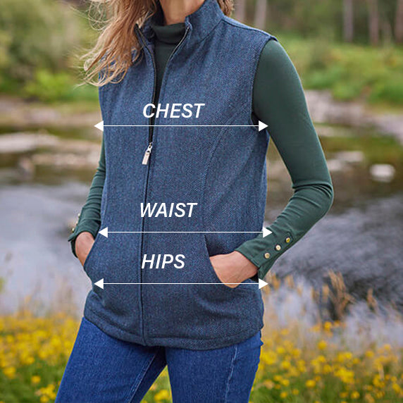 A woman stands outdoors beside a body of water, wearing a zip-up vest over a long-sleeve top. The image highlights measurement lines labeled
