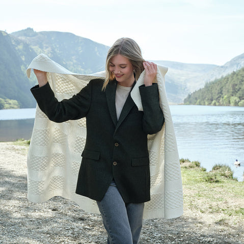 Woman holding a white blanket outdoors with mountains and water in the background