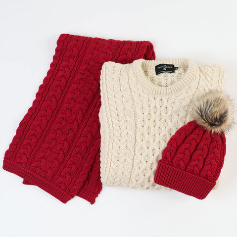 Close-up detail of a cream Aran sweater with red scarf and hat showing traditional Irish cable knit patterns and texture, perfect for festive winter occasions