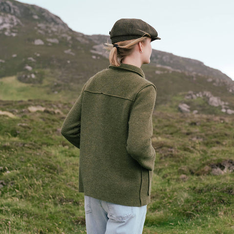 Back view of the Women's Irish Tweed Overshirt Jacket in olive green, crafted from authentic Irish tweed with a timeless overshirt silhouette, structured collar, and clean tailored lines, showcased against a scenic Irish countryside backdrop.