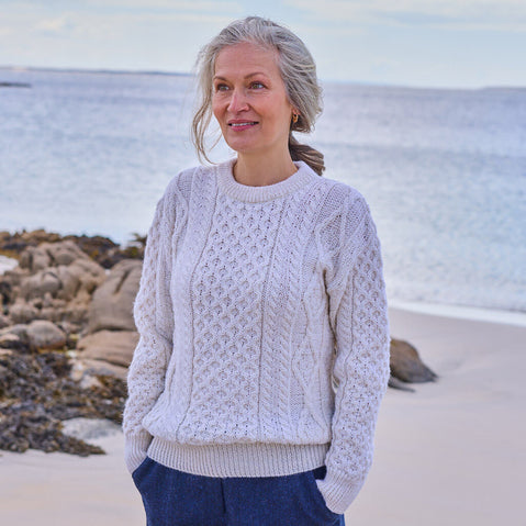 Woman wearing a cream Aran sweater standing on a beach with ocean in the background