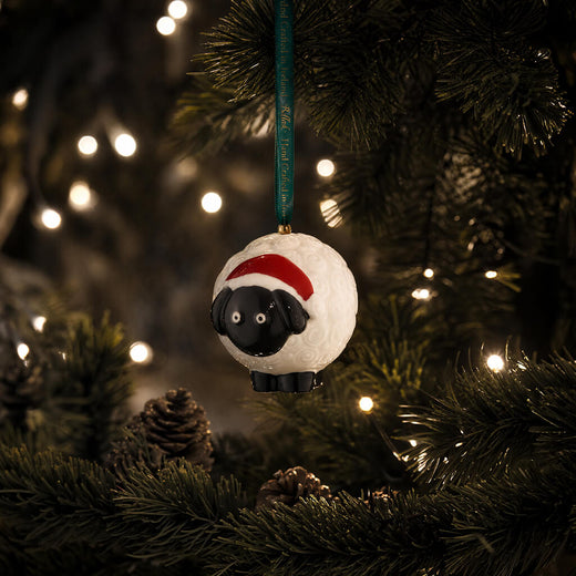 Belleek Kive sheep Christmas ornament with Santa hat hanging on decorated tree
