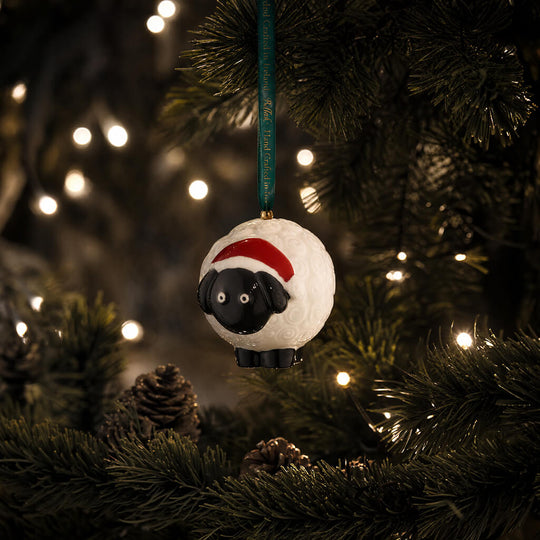 Belleek Kive sheep Christmas ornament with Santa hat hanging on decorated tree