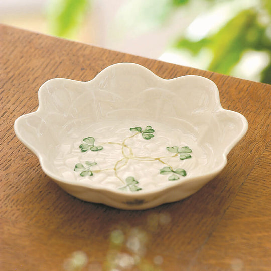 A white conical Belleek Shamrock sweet dish with a basketweave design and hand painted shamrocks pattern, placed on a wooden surface.
