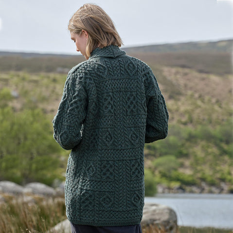 Person wearing a green Aran cardigan standing in a scenic outdoor setting with a lake and mountains.