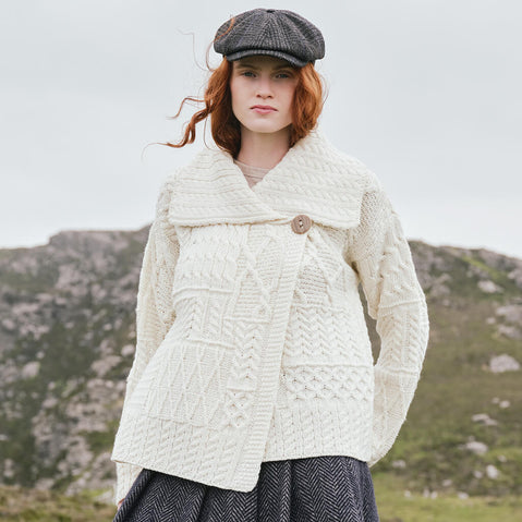 Image featuring the Women's One Button Aran Cardigan in cream, crafted with authentic Irish Aran cable knit patterns, a statement shawl collar, and classic one-button closure, showcasing timeless Irish craftsmanship in a scenic countryside setting.