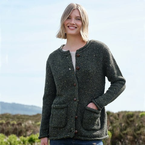 Woman wearing a dark green Aran cardigan outdoors with a blurred natural background