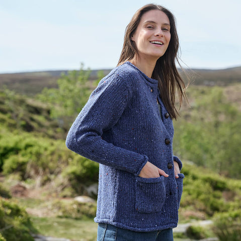 Woman wearing a blue Aran cardigan standing outdoors with greenery in the background