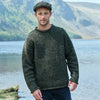 Man wearing a green Men's Traditional Fisherman Irish Wool Sweater standing by a lake with mountains in the background