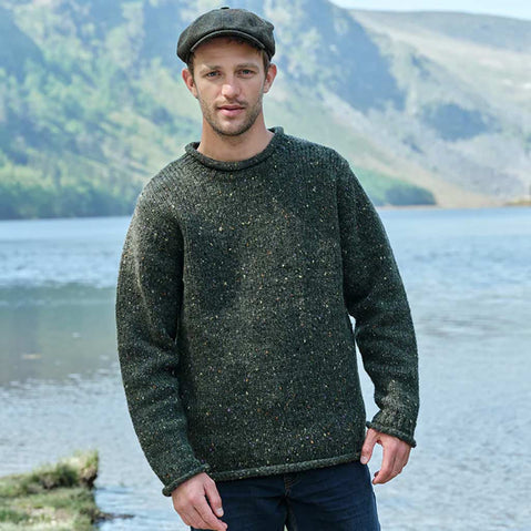 Man wearing a green Men's Traditional Fisherman Irish Wool Sweater standing by a lake with mountains in the background