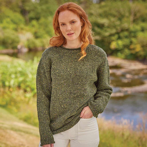 Woman wearing a green Women's Traditional Fisherman Irish Wool Sweater standing outdoors by a stream.