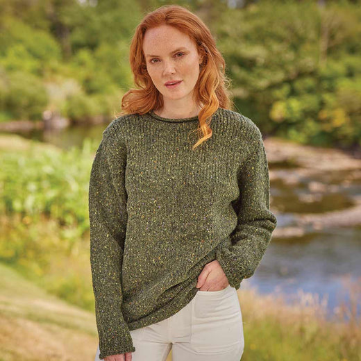 Woman wearing a green Women's Traditional Fisherman Irish Wool Sweater standing outdoors by a stream.