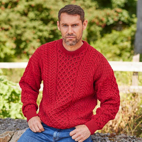 Man wearing a red knitted sweater outdoors with greenery in the background