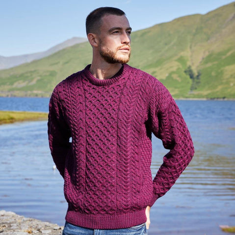 Man wearing a purple sweater standing by a lake with mountains in the background