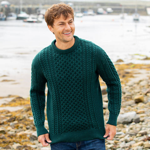 Man wearing a green sweater standing on a rocky beach.