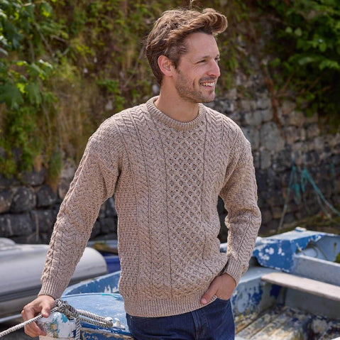 Smiling man wearing a beige Aran sweater standing near boats and greenery