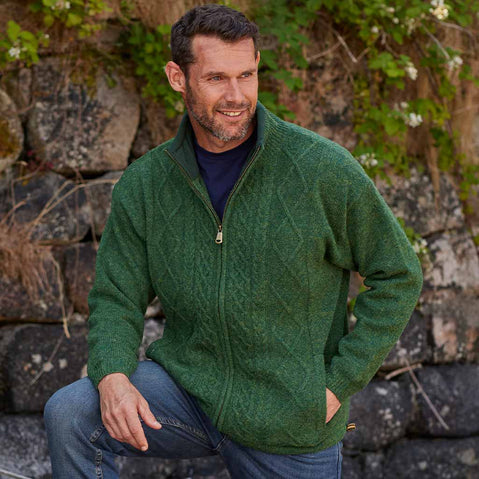 Man wearing a green Men's Signature Lined Fisherman Zipper Cardigan sitting against a stone wall with greenery.