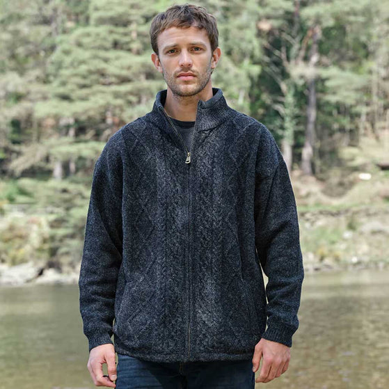 Man wearing a charcoal Men's Signature Lined Fisherman Zipper Cardigan standing by a body of water with trees in the background