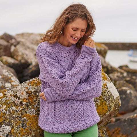 Woman wearing a purple knitted sweater standing on rocks with a blurred background