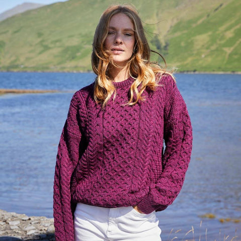 Woman wearing a purple knitted sweater by a lake with green hills in the background