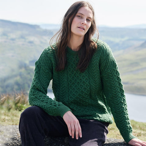 Woman wearing a green sweater sitting outdoors with a scenic background