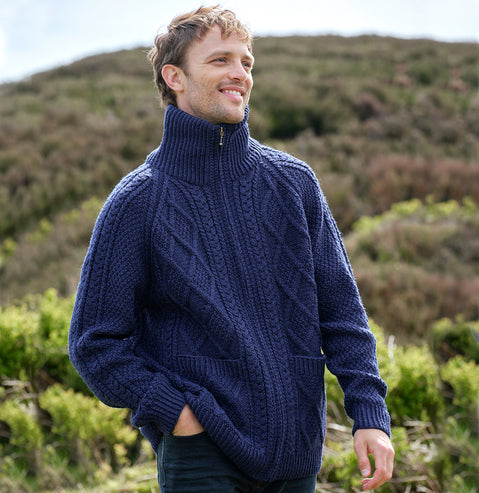 Man wearing a navy Men's Hand Knit Aran Zipper Cardigan standing in a natural landscape