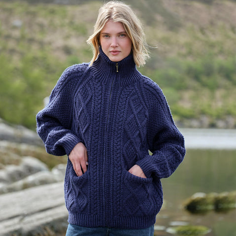 Woman wearing a navy Women's Hand Knit Aran Zipper Cardigan standing by a lake with mountains in the background
