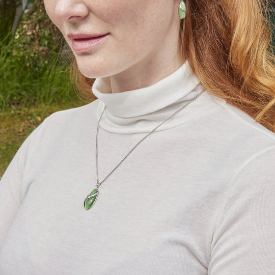 A woman wearing a white turtleneck sweater showcasing a Claddagh pendant necklace and matching earrings with a green cat's eye stone.