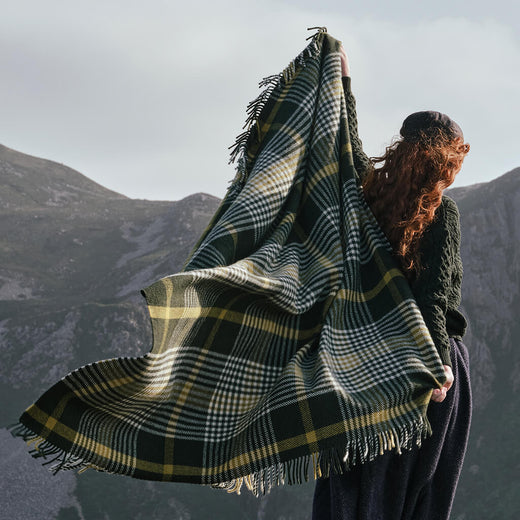Image featuring the Foxford Michael Collins Wool Throw, crafted from luxurious wool with a timeless green, cream, and gold check pattern and fringed finish, inspired by Irish heritage and showcased against a rugged countryside backdrop.