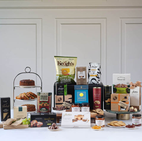 The Celtic Gourmet Food Gift Basket. Assorted Irish food products including chocolates, breads, and other baked goods on a white surface with a neutral background.