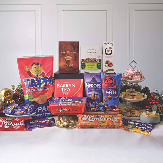 Assorted snacks and treats including Tayto, Barry Tea, and Heroes on a white surface with a festive background.