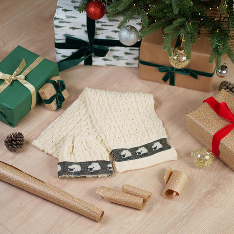 Aran Sheep Scarf - Cream cable knit scarf with grey sheep pattern border displayed with holiday gifts and Christmas decorations
