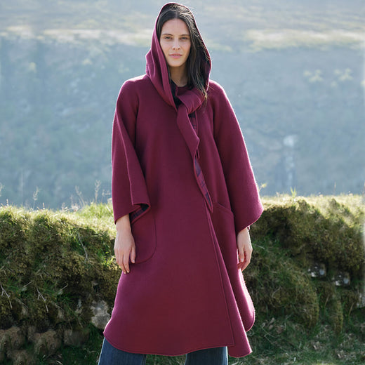 Woman wearing a burgundy hooded coat standing in a natural setting with greenery.