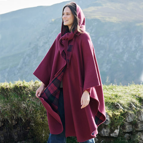 Woman wearing a red hooded cloak with plaid lining in a mountainous landscape