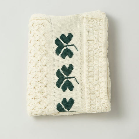 A folded Irish wool shamrock baby blanket with traditional Aran honeycomb stitching and a shamrock trim in moss green on a white background.