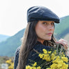 Woman wearing a flat cap holding yellow flowers with mountains in the background